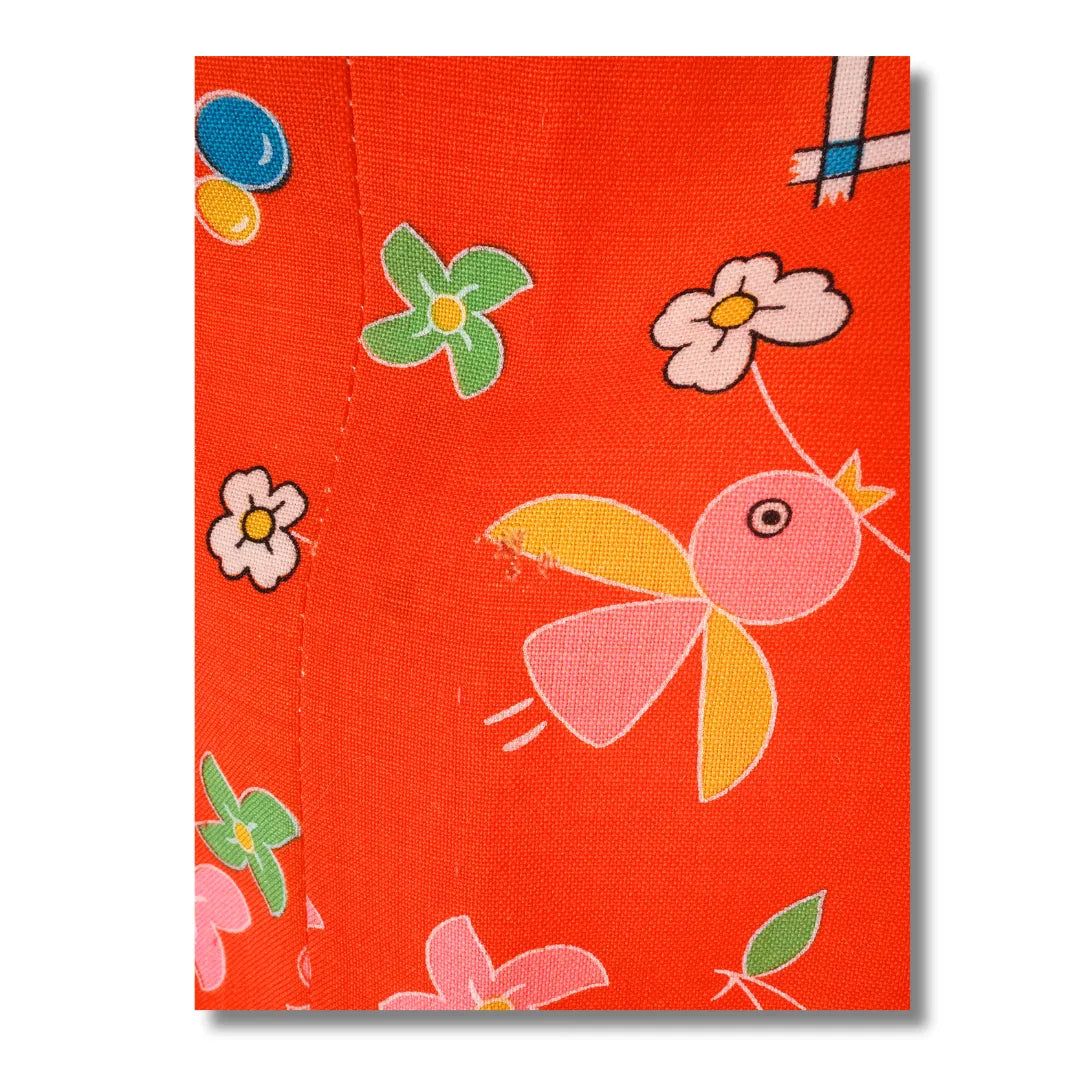 Detailaufnahme des bunten Musters mit Blüten und geometrischen Motiven auf rotem Stoff, mit Loch