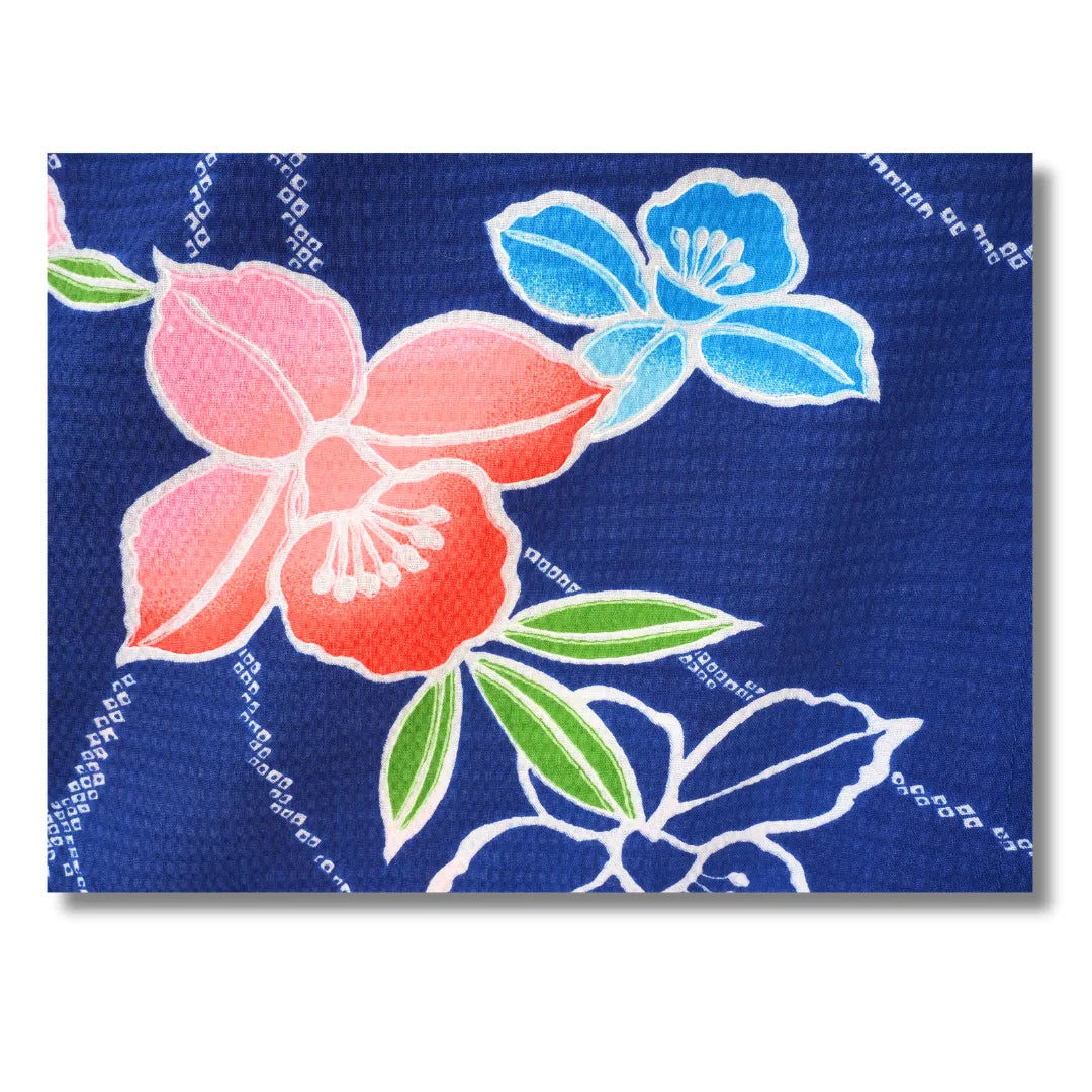 Großformatige Nahaufnahme einer pinken Kamelie mit Blättern auf marineblauem Kimono-Stoff