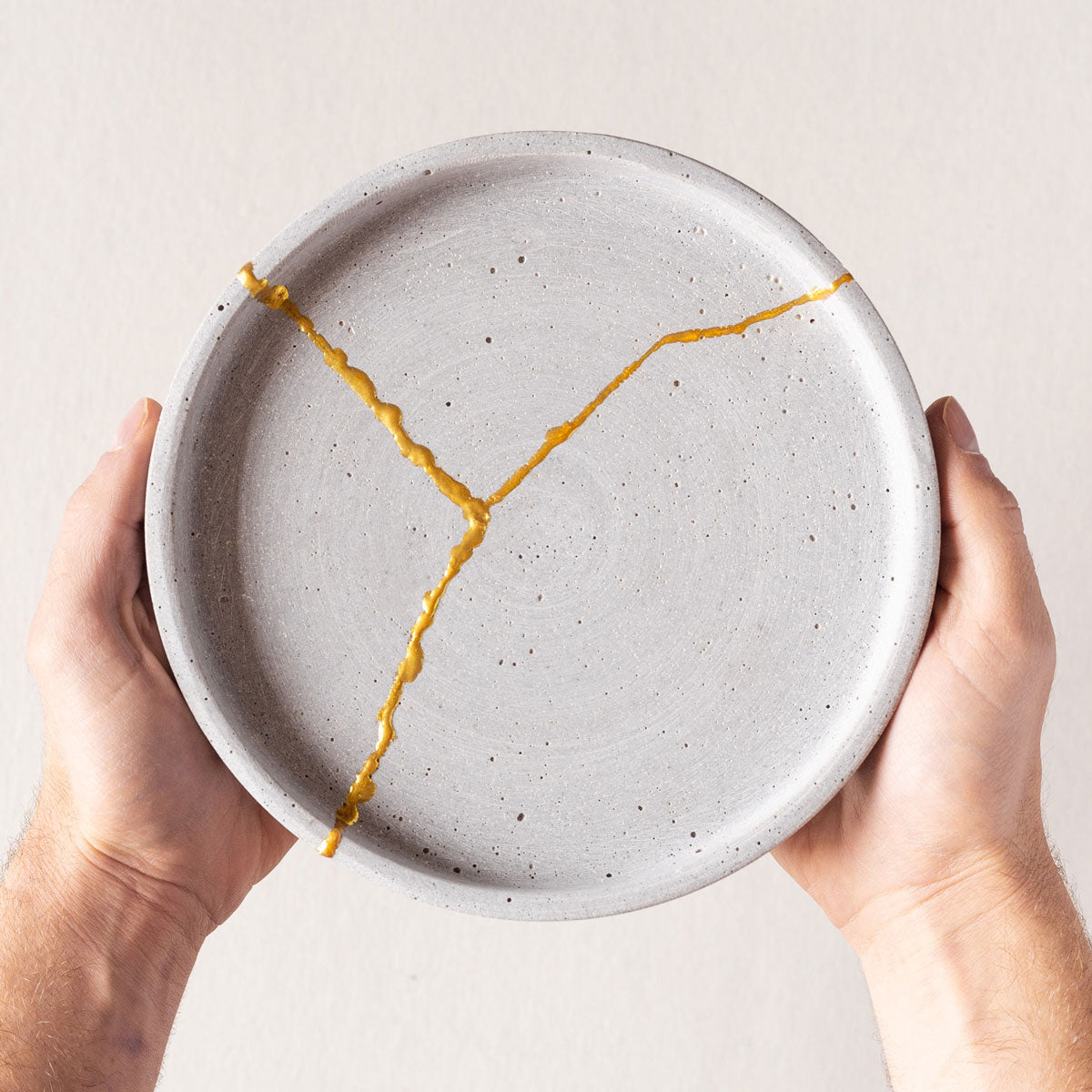 reparierter Kintsugi Teller wird in Händen gehalten #farbe_Gold
