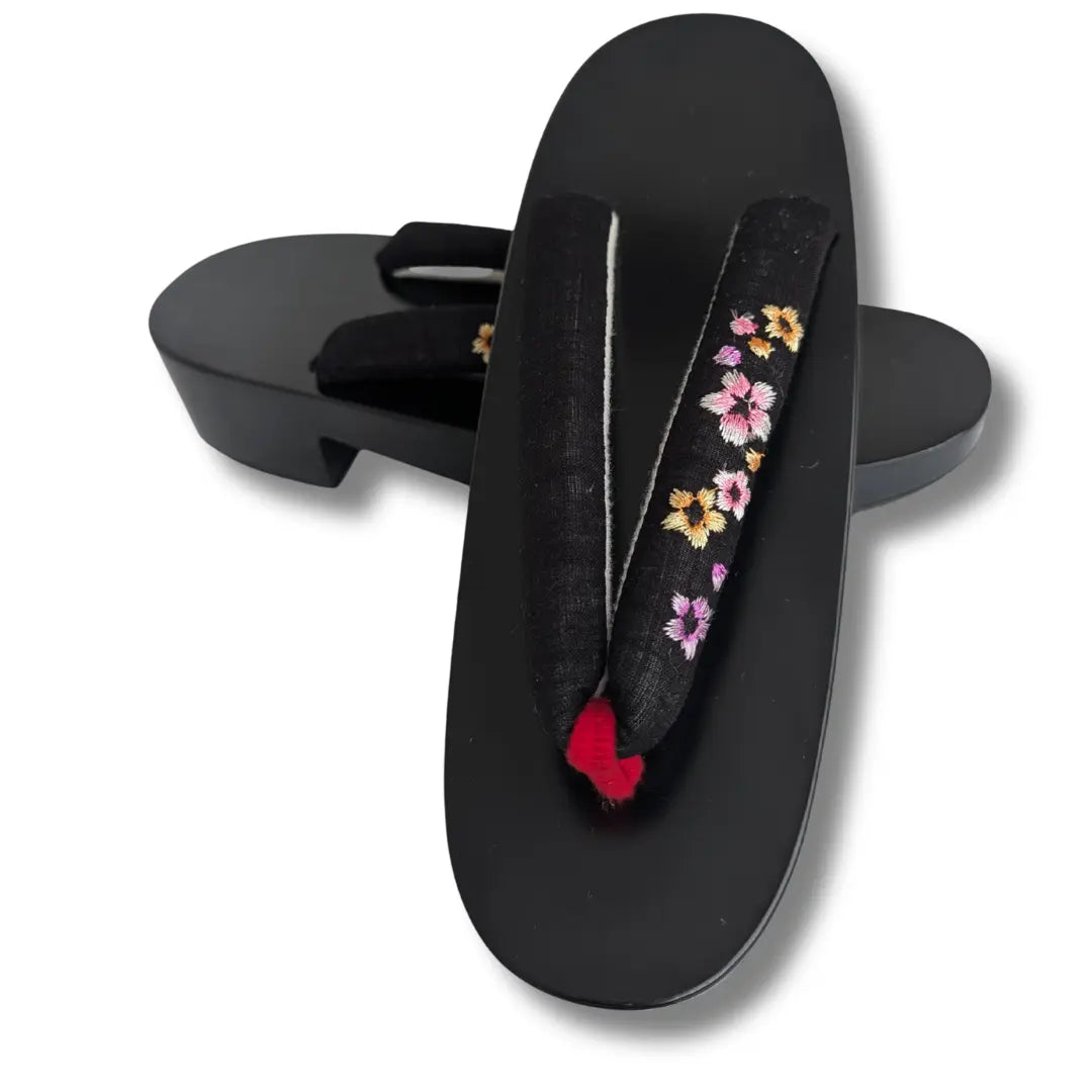 Schwarze Geta aus Paulownienholz mit bestickten Sakura-Riemen in Rosa und Gold