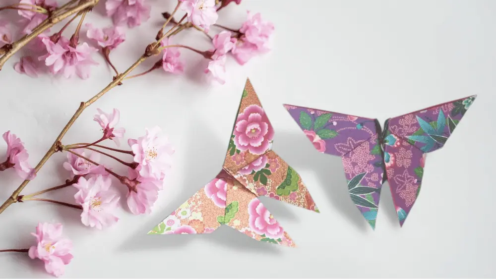 2 Origami Schmetterlinge neben Blumen